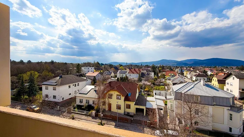 Panoramablick vom Balkon über eine Wohnsiedlung mit Bergen im Hintergrund unter blauem Himmel.