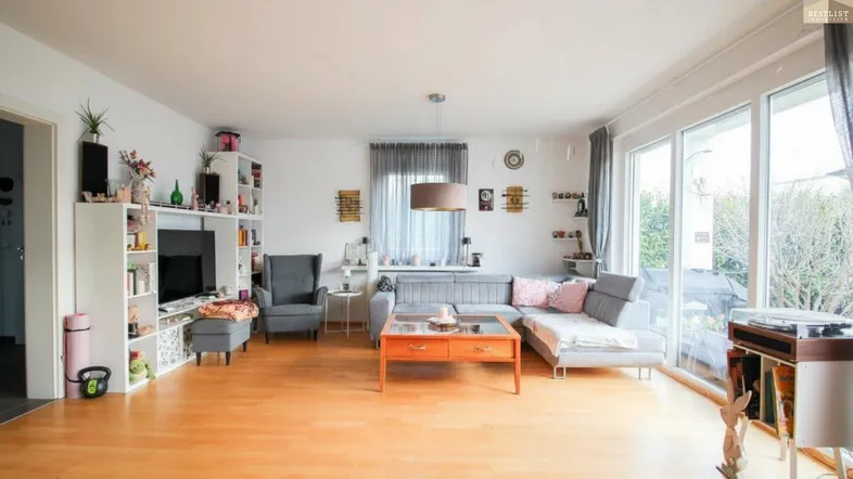 Helles Wohnzimmer mit gemütlichem Sofa, Holzboden und großen Fenstern zum Außenbereich.