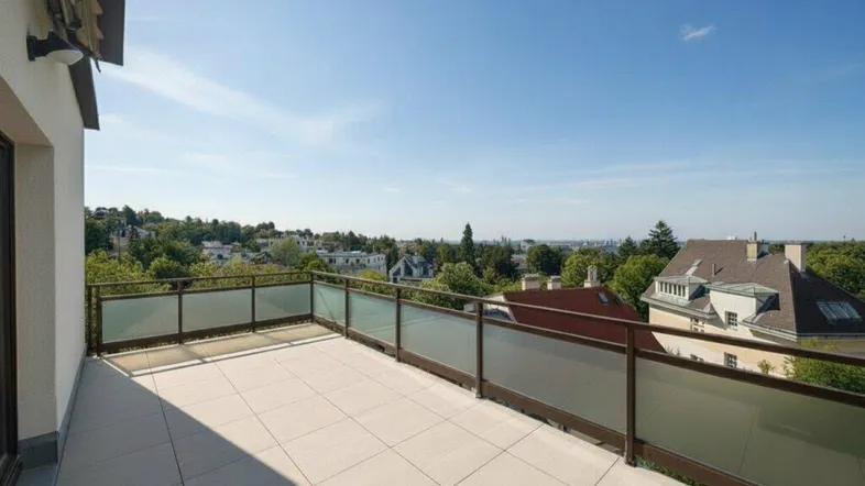 Große, geflieste Terrasse mit Glasgeländer und weitem Blick über die grüne Umgebung unter blauem Himmel.