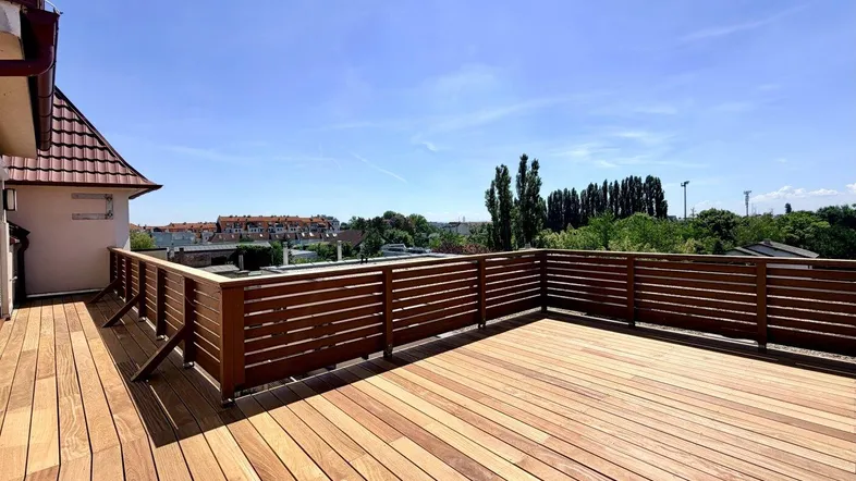 Große Holzterrasse mit modernem Geländer und weitem Blick unter blauem Himmel.