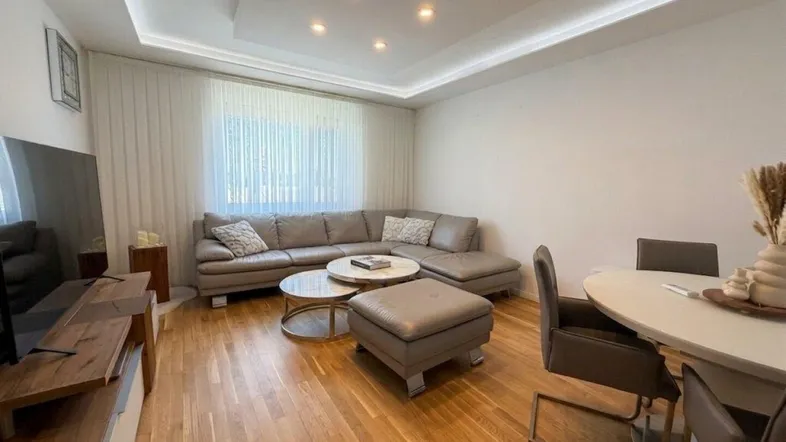 Heller Wohn- und Essbereich mit beigem Ledersofa, Holzboden und moderner Deckenbeleuchtung.