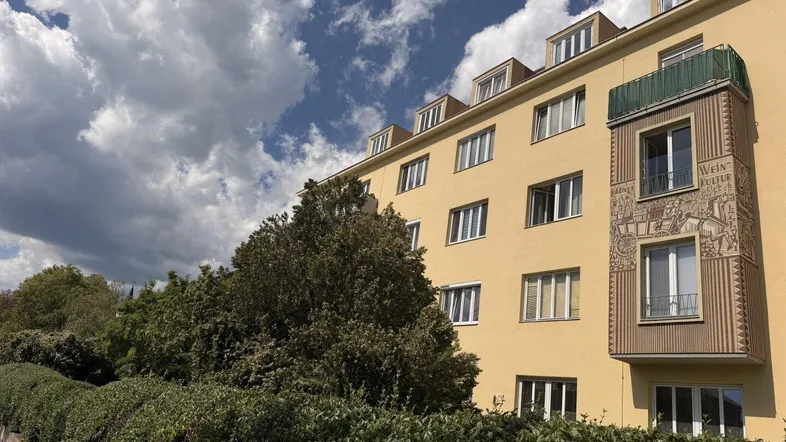 Gelbe Fassade eines Mehrfamilienhauses mit dekorativem Erker und Dachgauben unter blauem Himmel.