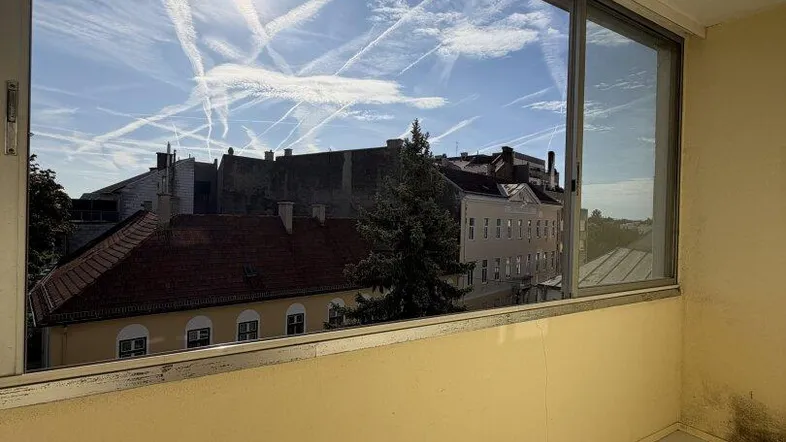 Heller Balkon mit Fliesenboden und Blick auf die umliegenden Stadtgebäude unter blauem Himmel.