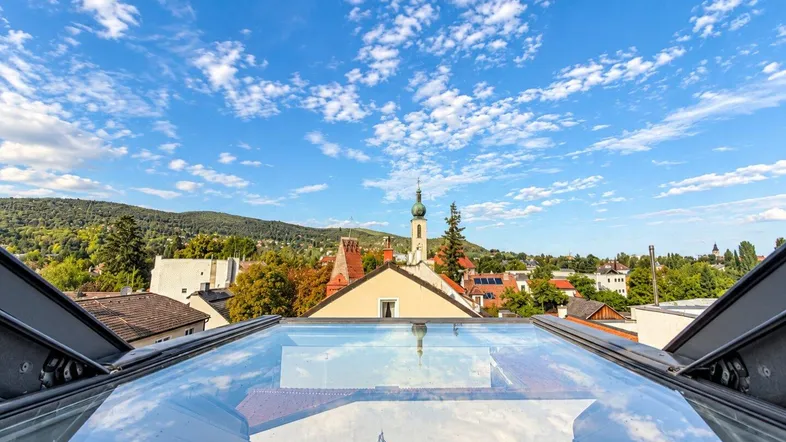 Panoramablick über die Stadt mit Kirchturm und grünen Hügeln unter blauem Himmel.