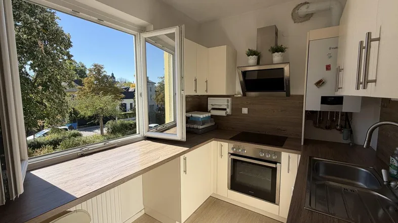 Helle Küche mit Holzarbeitsplatten, Einbaugeräten und einem großen Fenster mit Blick ins Grüne.