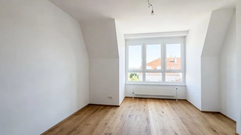 Helles Zimmer mit Holzboden und Dachschrägen, ideal als Schlaf- oder Wohnbereich nutzbar.