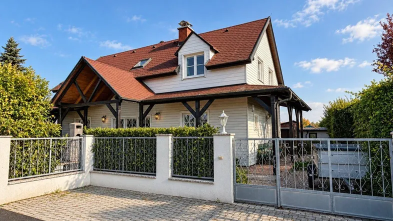 Charmantes Einfamilienhaus mit weißer Fassade, rotem Dach und gepflegtem Vorgarten unter blauem Himmel.