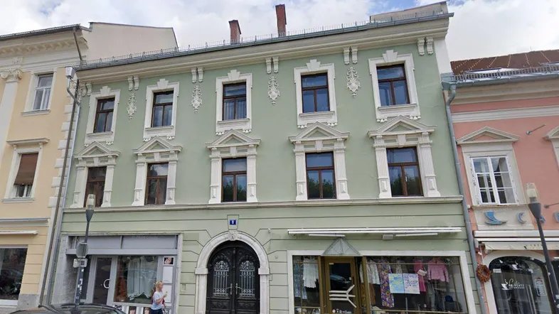 Historische Fassade eines Mehrfamilienhauses mit dekorativen Fensterrahmen und Geschäften im Erdgeschoss.