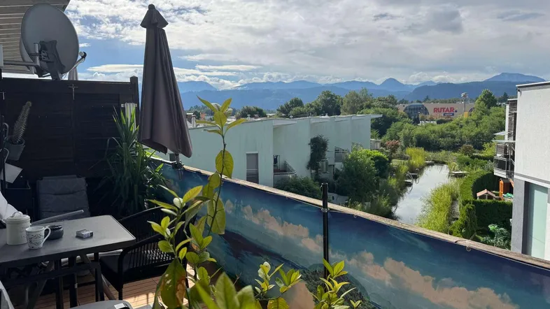 Gemütlicher Balkon mit Sitzgelegenheiten, Pflanzen und malerischem Blick auf Berge und Wasser.