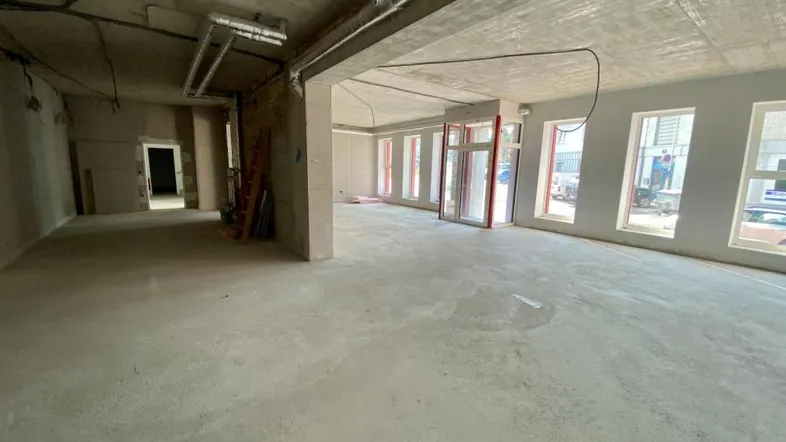 Großer, unfertiger Gewerberaum mit hohen Decken, Betonboden und großen Fenstern, die viel Tageslicht hereinlassen.