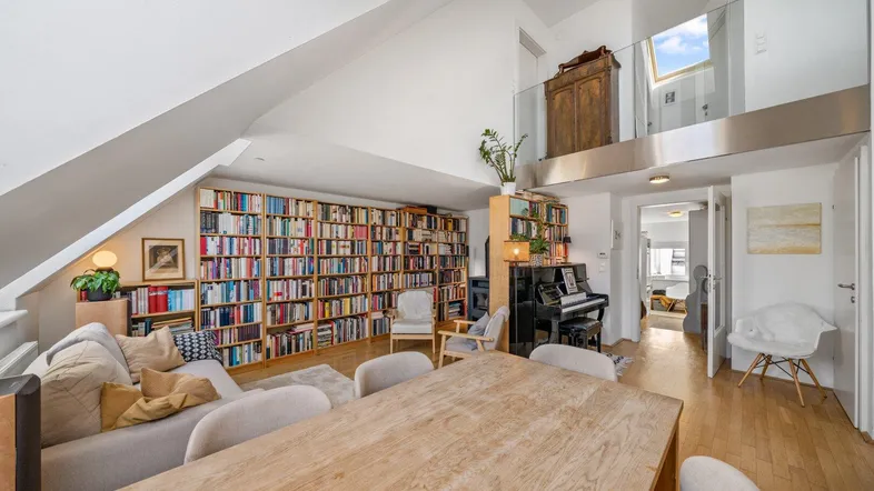 Geräumiger Wohn- und Essbereich mit hohen Decken, Bücherregalen und Zugang zu einer Galerie.