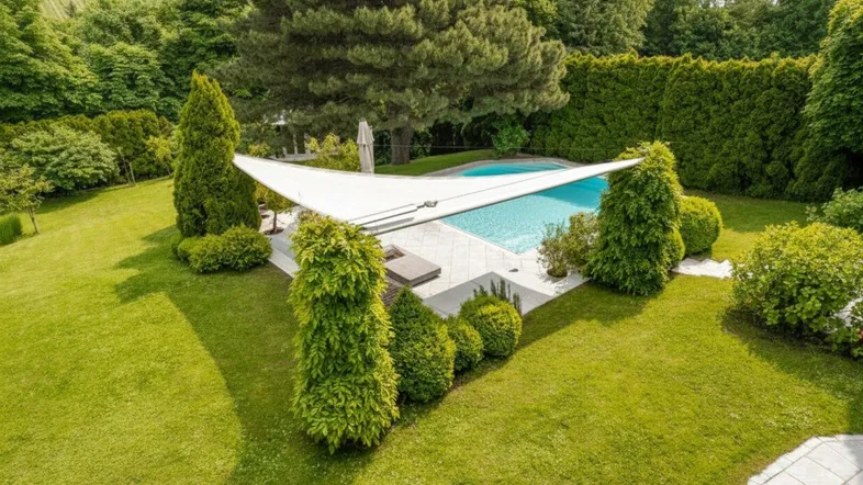 Großer Gartenbereich mit gepflegtem Rasen, einem Swimmingpool und üppiger Bepflanzung unter blauem Himmel.