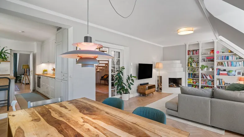 Geräumiger Wohn- und Essbereich mit Holztisch, Fischgrätparkett und Blick in die Küche.