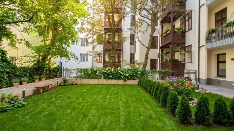 Gepflegter Gemeinschaftsgarten mit Rasenfläche und Bäumen, umgeben von Wohngebäuden.