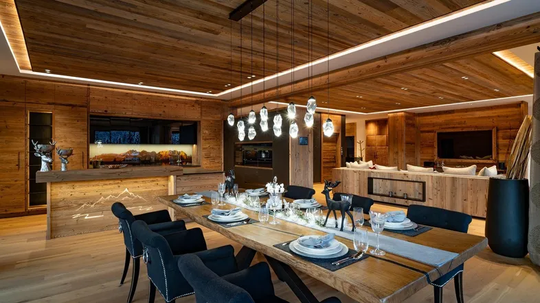 Geräumiger Wohn- und Essbereich im alpinen Stil mit Holzelementen, modernem Esstisch und integrierter Küche.
