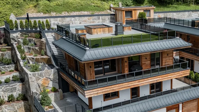 Moderne Architektur mit Holzfassaden, terrassierten Gärten und Flachdächern in einer grünen Hanglage.