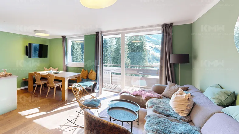 Helles Wohn- und Esszimmer mit Holzboden, gemütlicher Sitzecke und Zugang zum Balkon mit Bergblick.