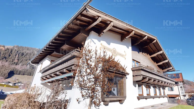 Traditionelles Gebäude im alpinen Stil mit Holzbalkonen und Satteldach, umgeben von Natur.