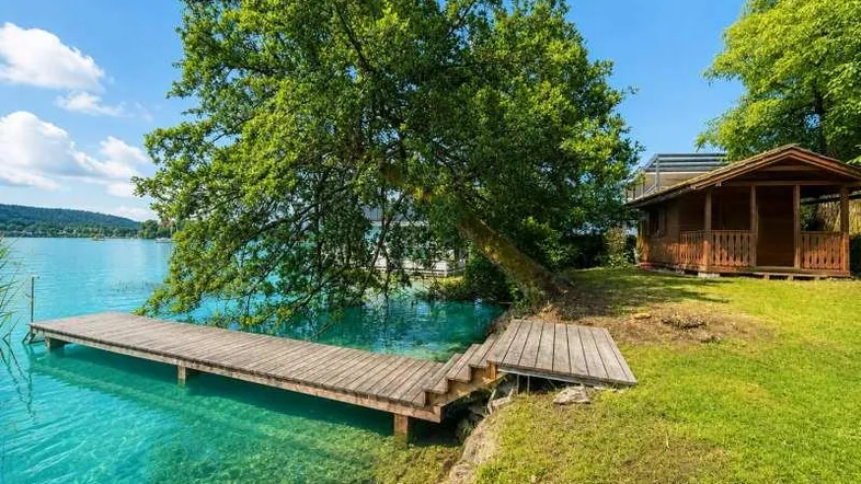 Idyllische Seelandschaft mit privatem Holzsteg, klarem Wasser und einer kleinen Holzhütte am Ufer.
