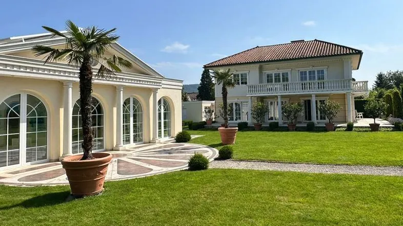 Großzügiger Gartenbereich mit gepflegtem Rasen, Palmen und zwei eleganten Gebäuden unter blauem Himmel.