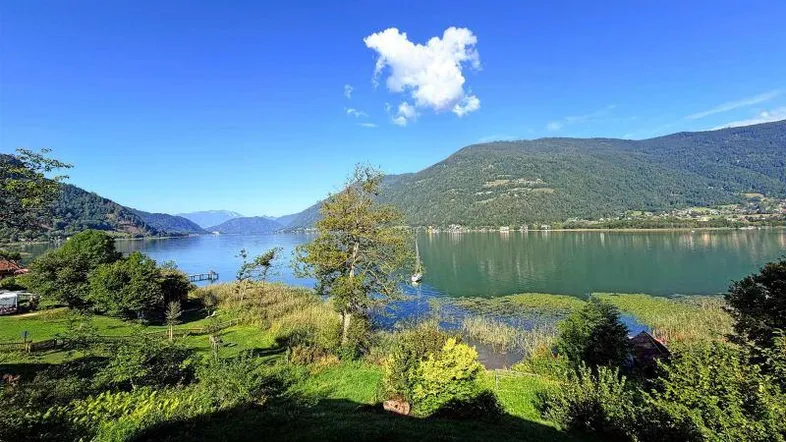 Panoramablick auf einen malerischen See, umgeben von grünen Bergen unter strahlend blauem Himmel.