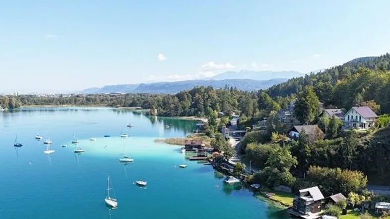 Panoramablick auf den See mit Segelbooten, umgeben von grünen Hügeln und Häusern am Ufer.