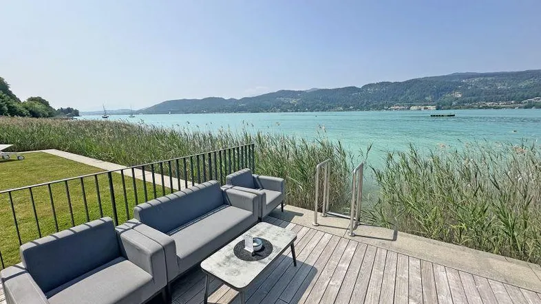 Moderne Holzterrasse mit bequemen Sitzmöbeln und direktem Zugang zum See mit Bergblick.