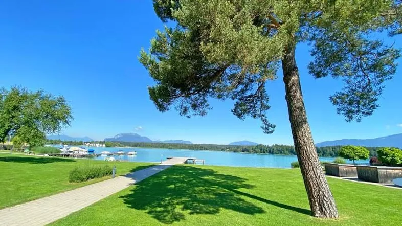 Idyllischer Blick auf den Faakersee mit grünen Ufern und majestätischen Bergen im Hintergrund.
