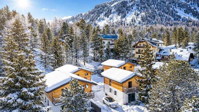 Winterlandschaft mit mehreren schneebedeckten Chalets und verschneiten Bäumen in den Bergen.