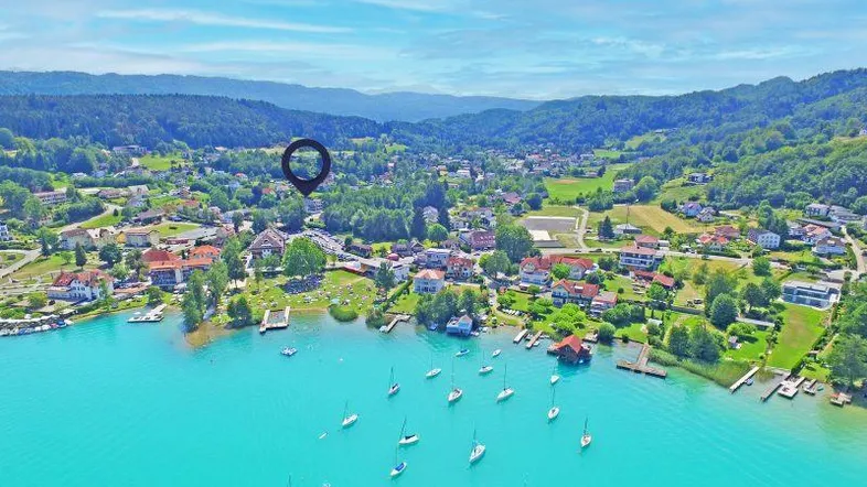 Luftaufnahme einer malerischen Seenlandschaft mit einem Dorf am Ufer, umgeben von grünen Hügeln und Bergen.