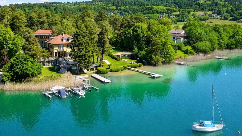 Luftaufnahme eines weitläufigen Anwesens am See mit mehreren Gebäuden, Stegen und üppiger Vegetation.