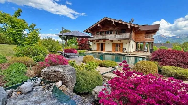 Großzügiger Gartenbereich mit Pool, Liegewiese und vielfältiger Bepflanzung vor alpiner Kulisse.