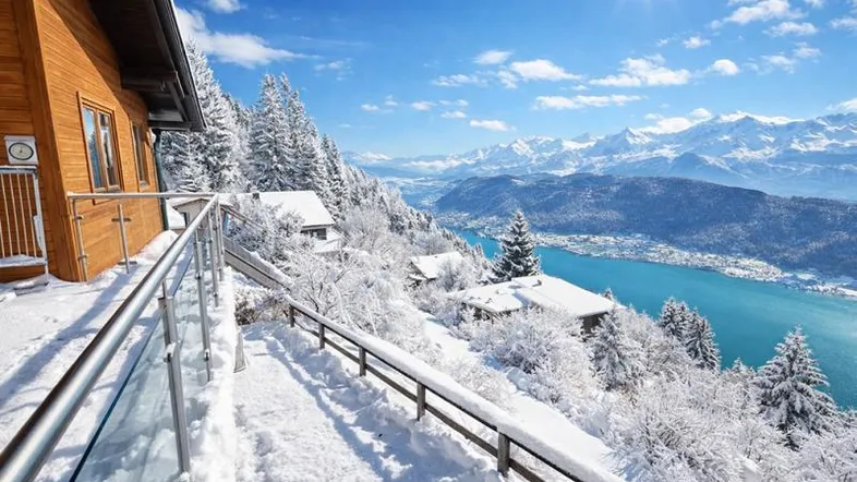 Sonniger Balkon mit Glasgeländer und atemberaubendem Blick auf den See und die verschneiten Berge.