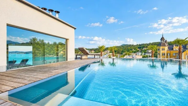 Luxuriöser Infinity-Pool auf dem Dach mit Holzdeck, Seeblick und Bergszenerie im Hintergrund.