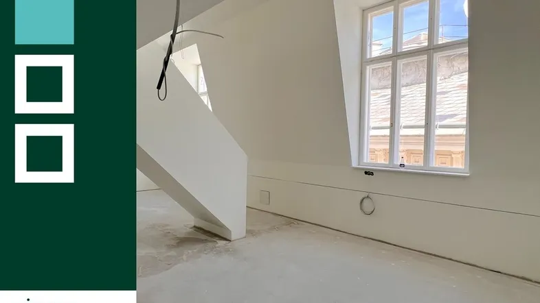 Heller Dachbodenraum im Rohbau mit schrägen Wänden und großen Fenstern, bereit für den Ausbau.