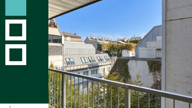 Geräumiger Balkon mit Holzboden und Blick auf die umliegenden Gebäude und Bäume unter blauem Himmel.