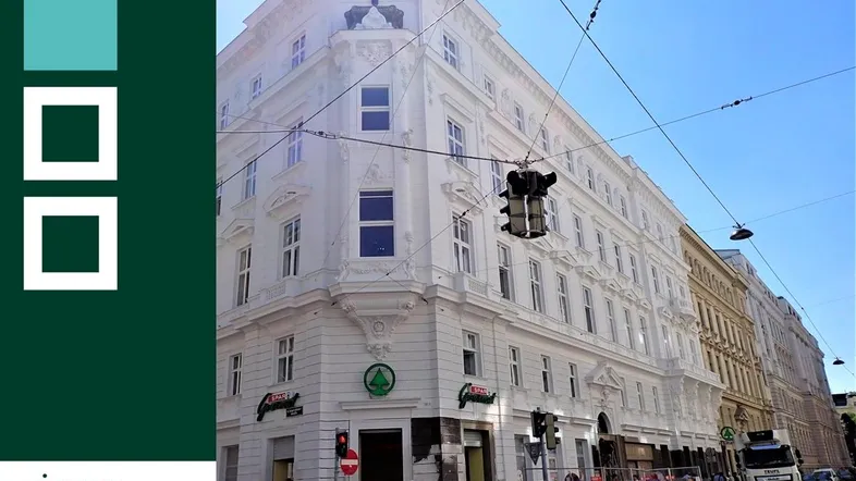 Weißes Eckgebäude mit klassischer Architektur und Geschäften im Erdgeschoss in einer städtischen Umgebung.