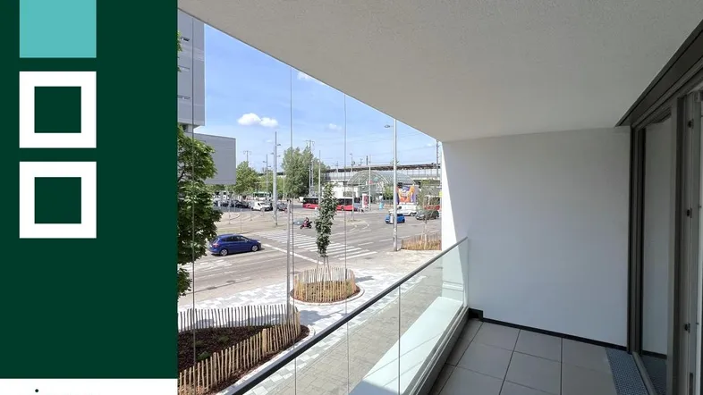 Heller Balkon mit Glasgeländer und Blick auf die Straße und umliegende Gebäude.