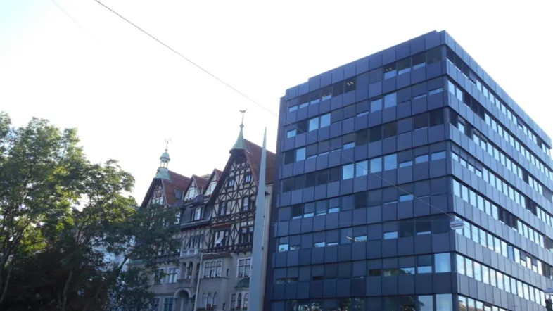 Die Aufnahme zeigt eine moderne Bürogebäude-Fassade neben einem traditionellen Altbau mit Fachwerkelementen.
