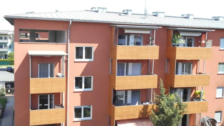 Mehrfamilienhaus mit mehreren Balkonen und moderner Fassadengestaltung in warmen Farbtönen.