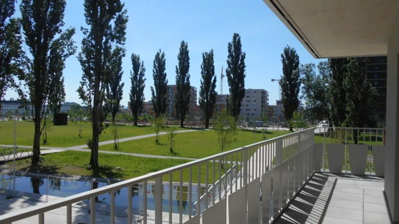 Geräumiger Balkon mit Blick auf eine grüne Parklandschaft und moderne Gebäude.