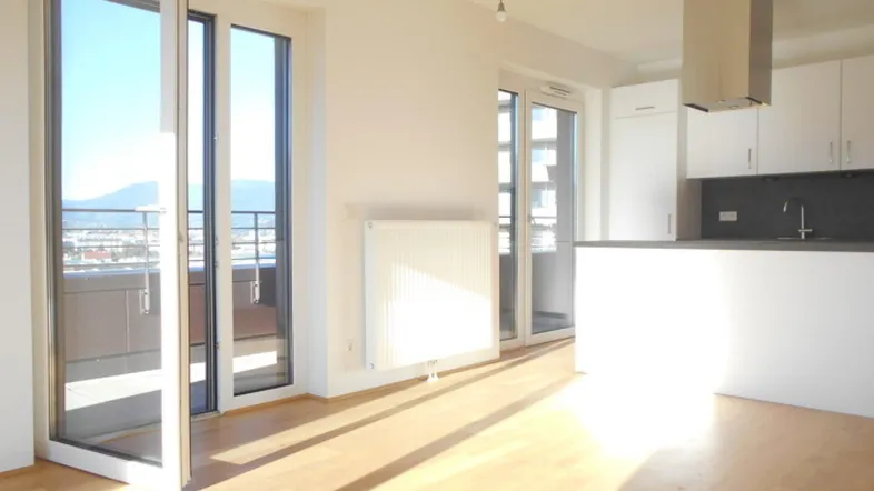Heller offener Wohn-Essbereich mit integrierter Küche, Parkettboden und Zugang zu einem Balkon mit Bergblick.