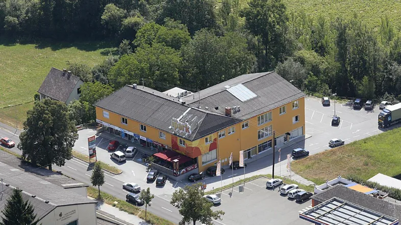 Luftaufnahme eines großen Gewerbegebäudes mit Parkplätzen und umgeben von viel Grün.