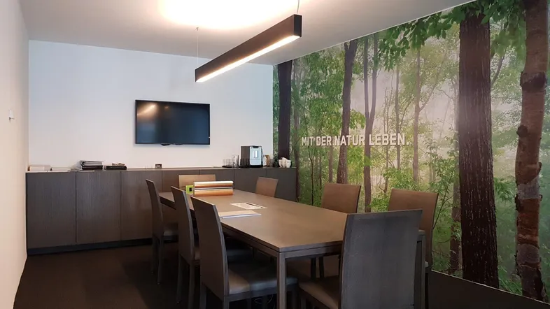 Moderner Konferenzraum mit großem Tisch, bequemen Stühlen und einer beeindruckenden Waldtapete, die eine natürliche Atmosphäre schafft.