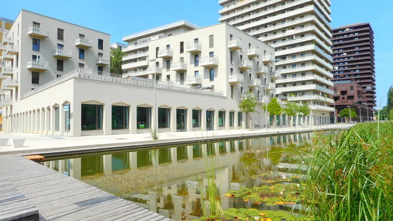Moderne Wohngebäude mit Balkonen und einer Wasseranlage im Vordergrund unter blauem Himmel.