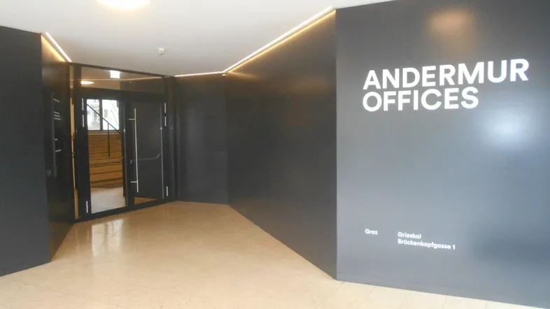 Moderner Eingangsbereich mit dunklen Wänden, heller Fliesenboden und indirekter Beleuchtung, der zu den Andermur Offices führt.