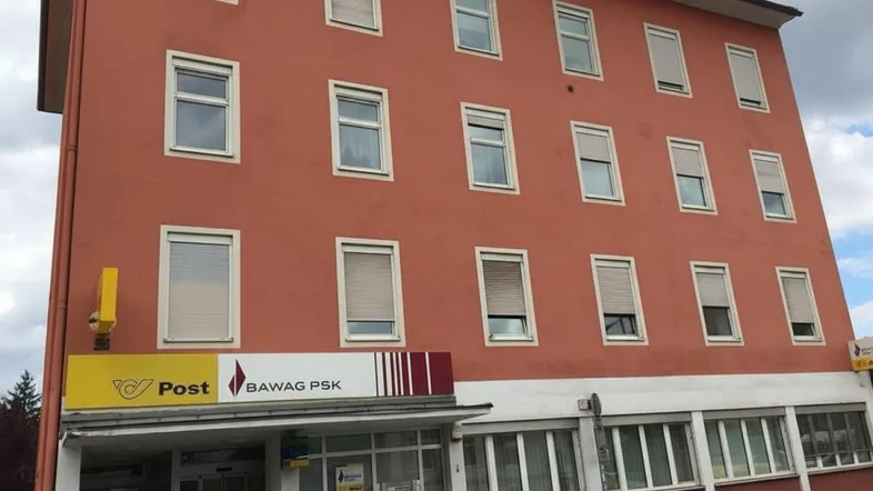 Mehrstöckiges Gebäude mit oranger Fassade und vielen Fenstern, im Erdgeschoss befindet sich eine Postfiliale.