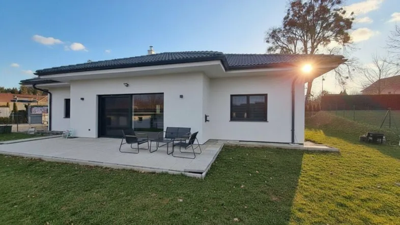 Modernes Einfamilienhaus mit sonniger Terrasse, Gartenmöbeln und gepflegtem Rasen.