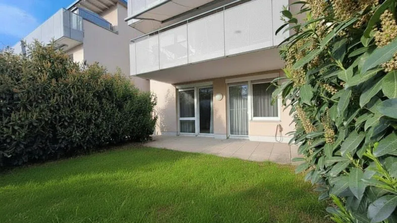 Erdgeschosswohnung mit privater Terrasse und kleinem Gartenbereich, umgeben von grünen Hecken und moderner Architektur.