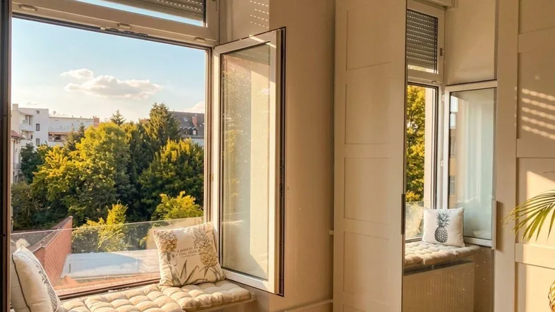 Gemütlicher Fensterplatz mit Kissen und Blick ins Grüne, durchflutet von warmem Sonnenlicht.